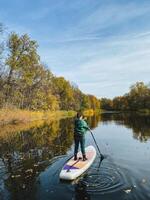 A person is enjoying a leisurely ride on a paddle board as they glide along the surface of a serene river, surrounded by the beauty of nature and the calming sounds of water photo