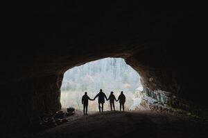 A diverse group of individuals is present in a dimly lit cave, standing closely together and holding hands in a gesture of unity and support, amidst the natural rocky landscape around them photo