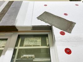 This is a detailed closeup view that showcases the application process of exterior insulation on a building at a busy construction site, highlighting craftsmanship photo