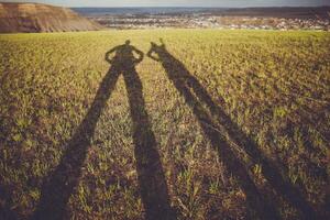 Two People Are Standing In A Field With Their Shadows On The Grass photo