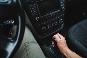 The person in the car is manually changing gears while driving by operating the gear shifter. This process takes place inside the vehicle, requiring the drivers attention and skill photo