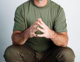 A man is wearing a bright green shirt while sitting comfortably, with his hands folded in a precise triangle shape, which conveys a strong sense of relaxation and ease in his entire posture photo