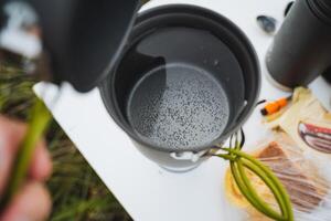 When camping outdoors, its essential to prepare water using a portable pot to elevate your cooking experience while fully enjoying natures beauty photo
