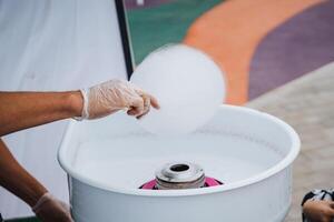 A talented individual adeptly operates a specialized machine that is designed to produce fluffy, sweet cotton candy, which is a beloved treat often enjoyed at fairs and exciting carnivals photo