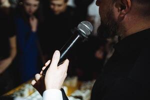 A man gestures with a microphone, performing for a crowd at a music event photo