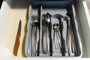 A drawer that is filled with various pieces of silverware, including an assortment of spoons, forks, and knives, each serving a specific purpose in the kitchen or dining area photo