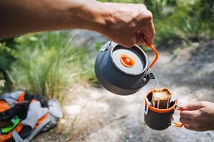 Elevate your camping experience with a hot beverage from a kettle, sipping it from a mug while hiking in nature on a beautiful trail, surrounded by greenery and serenity photo