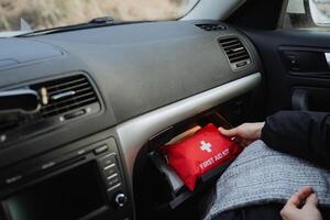 An individual is currently engaged in the process of retrieving a first aid kit from the glove compartment, which is situated in the front section of a parked vehicle, specifically a car photo