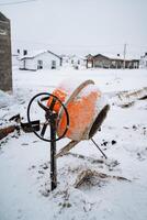 In the midst of a wintry landscape, an orange cement mixer is quietly sitting in the soft, white snow, surrounded by the chill of freezing temperatures, ice, and frosty air photo