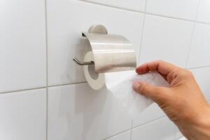 An individual is in the process of removing a roll of toilet paper from a dispenser that is specifically designed for holding toilet paper rolls and providing easy access to them photo