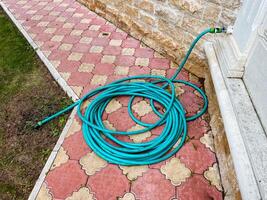 A long and vibrant green garden hose is neatly coiled and resting calmly on the sidewalk that runs parallel to a large building, catching the attention of those who pass by and admire it photo