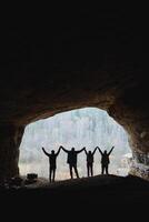 A group of people is standing together in a cave, holding hands in solidarity and friendship, creating a memorable moment in this unique and dark landscape of natures architecture photo