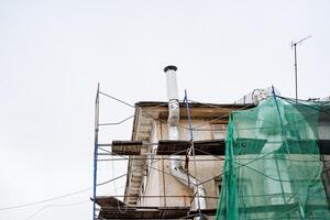 A large commercial building is currently undergoing extensive remodeling, surrounded by scaffolding and wrapped in a protective green net to ensure safety during the ongoing renovations photo