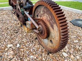 A large rusty gear is positioned atop a substantial pile of gravel, showcasing its weathered texture against the rough surface of the gravel below, highlighting its industrial significance photo