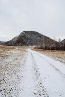 A snowy road gently winding its way through a vast open field, with a majestic mountain rising prominently in the background, creating a picturesque winter scene for travelers photo