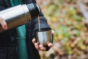 A person is skillfully pouring a steaming cup of coffee from a thermos into a white ceramic cup, showcasing their love for warm beverages during a possibly chilly morning or afternoon photo