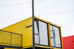A yellow shipping container, which features a balcony and several windows, is situated right next to a striking red shipping container, creating an interesting visual contrast photo