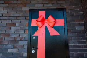 I notice a striking black door accented by a vibrant red bow, making it distinct against the brick building. The bold color contrast forms a powerful visual representation photo