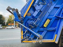 A blue garbage truck is currently parked over on the side of the road, waiting to fulfill its duty of collecting trash and keeping the area clean and tidy for the community photo