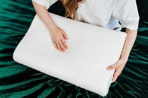 In a cozy bedroom, a woman enhances comfort and relaxation by holding an orthopedic memory foam pillow on a green velvet bedspread, creating a luxurious and modern setting photo