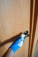 A meticulous individual is wearing blue hygiene gloves and is carefully cleaning a door handle with a napkin, ensuring that it is entirely free from germs, dirt, and any contaminants photo