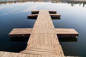 A wooden dock extends into a tranquil lake, surrounded by natures beauty, making it an ideal spot for enjoying a splendid outdoor day filled with fresh air and serenity photo
