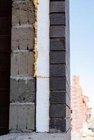 A brick wall with a piece of styrofoam stands against the sky, showcasing a mix of building materials and textures on the facade, including brickwork and composite materials photo