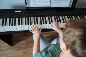 A young boy is happily playing a piano in a cozy living room, showcasing his musical talent and joy as he interacts with the instrument and enjoys creating beautiful melodies photo