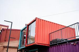 There is an eyecatching red and purple shipping container that features a balcony placed on top, creating a striking visual element in its overall design and architecture photo