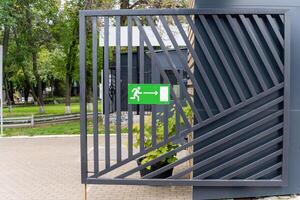 There is a metal gate that features a green exit sign clearly visible on it photo