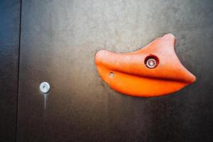 This image features a closeup view of an orange climbing grip that is attached to a wall. It provides a detailed look at the texture and color of the grip, highlighting its vibrant hue photo