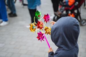 A joyful child wearing a cozy hoodie is gleefully spinning a vibrant and colorful windmill, fully enjoying the gentle and soft breeze that flows pleasantly through the fresh air photo