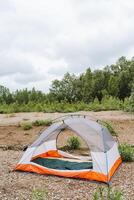 An orange and white tent is pitched in a picturesque natural setting under a cloudy sky, surrounded by lush greenery, ideal for camping and outdoor explorations photo
