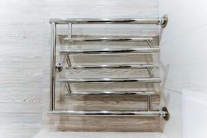 A metal towel rack with a rectangle handle sits on the bathroom floor photo