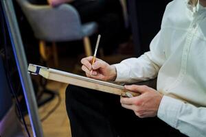 A man gestures with a brush and paper in front of an easel photo