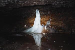 Stalactite ice formations can be discovered in a dark cave, where their stunning beauty is reflected on the surface of the water beneath them photo