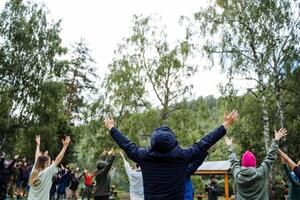 A group of people are joyfully gathered in a circle with their arms raised, participating in a recreational activity outdoors under the open sky, surrounded by nature and green grass photo