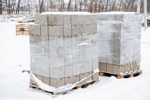 Two tightly wrapped pallets of bricks are sitting immobile in the cold, fluffy snow, standing out in stark contrast against the beautiful wintry landscape that surrounds them entirely photo