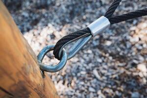This is a CloseUp View of a Metal Ring and a Cable Securely Fastened to a Wooden Post Within a Playground Setting Surrounded by Nature photo