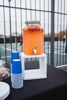 A spacious table in the room features a stylish drink dispenser and neatly arranged electric blue cups, ready to serve refreshing beverages for the guests of the gathering photo