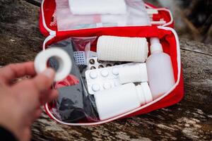 A person is currently holding a bandage while positioned right in front of an open first aid kit, suggesting readiness for any potential medical emergencies that may arise photo