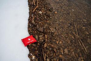 A bright red first aid kit has been inexplicably placed on the ground, creating a striking and vivid contrast against the surrounding elements of both nature and the urban scenery around it photo