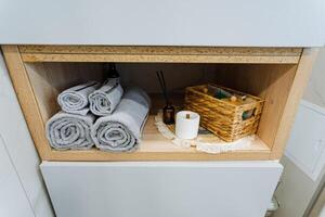 A wellorganized bathroom cabinet is expertly packed with neatly folded towels of various sizes, rolls of soft toilet paper, and an attractive basket that serves multiple storage purposes photo