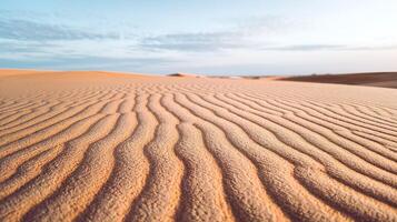 Golden Sand Dunes with Rippling Patterns Under Soft Light and Blue Sky Horizon in a Tranquil Desert photo