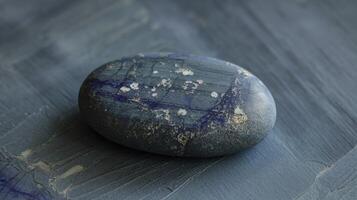 Smooth Oval Gray Stone with Blue and White Patterns on Textured Surface Light Background photo