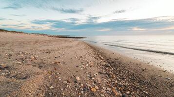 Serene Sandy Beach with Pebbles at Sunset with Calm Ocean Waves and Soft Clouds in the Sky photo