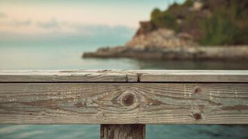 Closeup of weathered wooden pier with blurred blue sea rocky shore and green foliage background photo