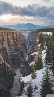 Snowy Canyon Landscape with Pine Trees River Deep Cliffs and Distant Mountains at Sunset photo