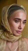 Elegant Woman Wearing Gold Sheer Fabric Headscarf with Subtle Makeup Against Textured Yellow Background photo