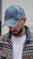 Man Wearing Distressed Blue Denim Cap and Jacket with Textile Pattern in Urban Light Background photo